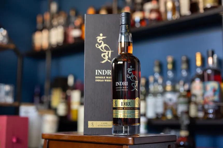 Indri Dru cask strength bottle beside its black presentation box on a bar counter